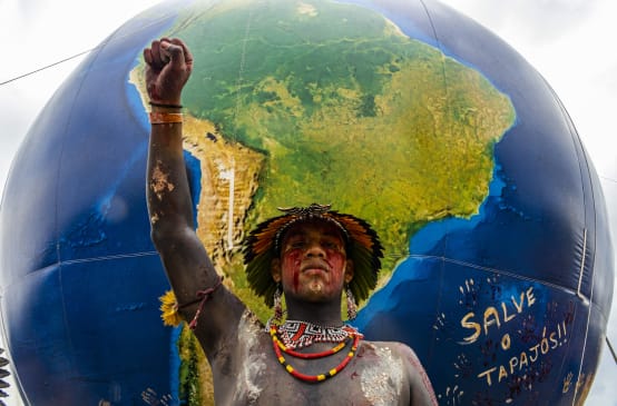 Indígena brasileiro com o punho erguido em frente a um globo mostrando a América do Sul