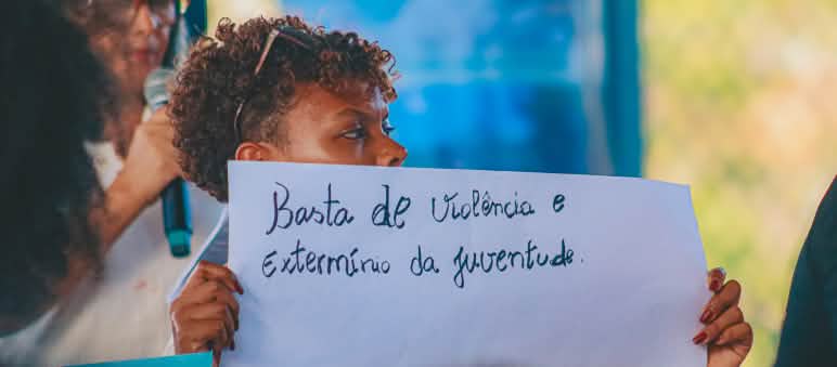 Jovens que participaram do congresso são egressos de oficina de comunicação popular realizada pela CPT Maranhão em parceria com Salve a Floresta Mulher jovem segura cartaz onde está escrito "Basta de violência e extermínio da juventude"
