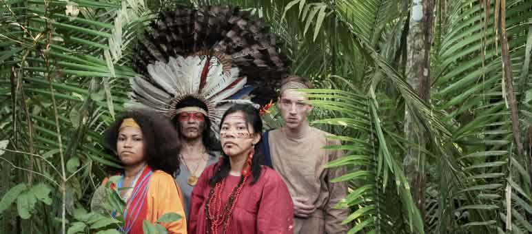 Cena da peça de teatro "Antígona na Amazônia" Atrizes e atores da peça de teatro “Antígona na Amazônia” em pé, na floresta amazônica