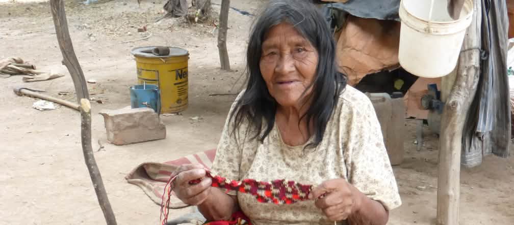 Os Manjui confeccionam utensílios e objetos artísticos com fibras vegetais. Mulher do povo Manjui sentada, trabalhando em um tecido à base de fibras vegetais