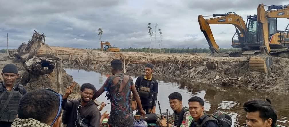 A devastação já começou: Escavadeira do Grupo Johnlin na aldeia Wanam, março de 2025 Escavadeira atrás de um grupo de homens
