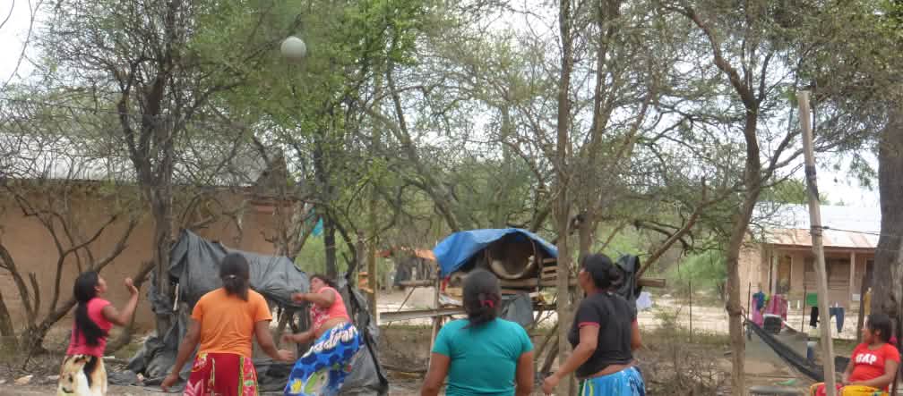Mulheres do povo Manjui na Colônia Santa Rosa, situada no Chaco paraguaio. Cinco mulheres indígenas jogando bola entre árvores e casas de madeira