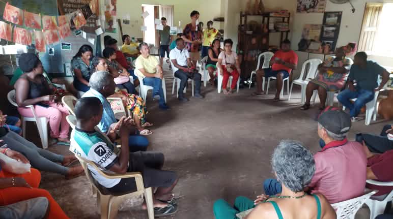Reunião realizada em abril de 2024 durante um intercâmbio entre povos e comunidades tradicionais na cidade de Alcântara, no Maranhão. Cerca de 25 pessoas sentadas em roda estão conversando sobre impactos de projeto porto-ferroviário. Estão em uma sala com algumas prateleiras de livros e fotos nas paredes.