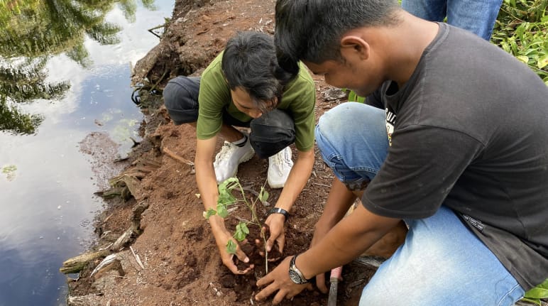 Dois homens plantando uma muda de árvore em um canal