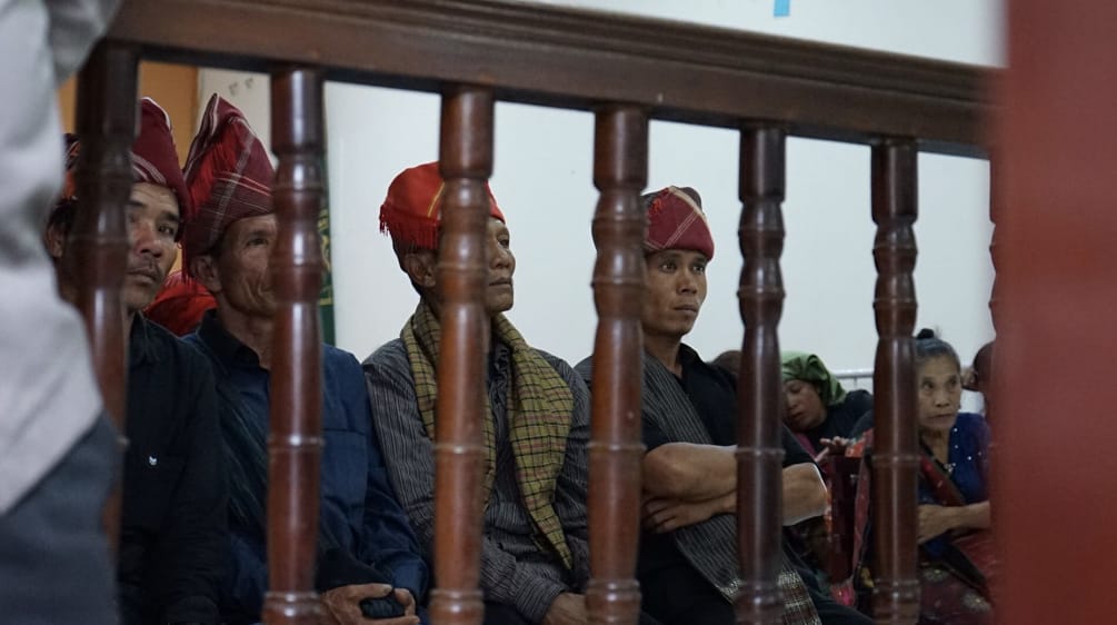 Homens com cabeças cobertas da forma típica dos Batak sentados atrás das grades